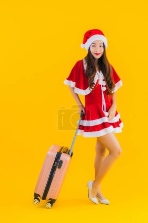 Foto de Retrato hermosa mujer asiática joven usar ropa de Navidad sombrero con bolsa de equipaje y teléfono inteligente listo para viajar sobre fondo aislado amarillo - Imagen libre de derechos