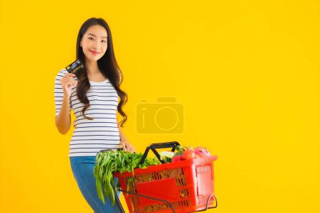 Photo for Portrait beautiful young asian woman shopping grocery cart from supermarket with credit card on yellow isolated background - Royalty Free Image