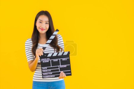 Photo for Portrait beautiful young asian woman show clapper movie board on yellow isolated background - Royalty Free Image