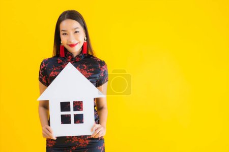 Photo for Portrait beautiful young asian woman wear chinese dress show home sign symbol on yellow isolated background - Royalty Free Image