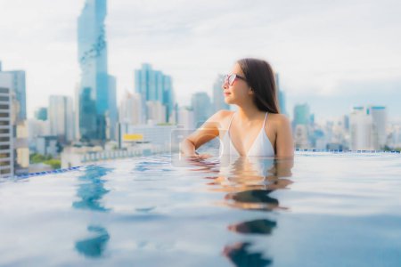 Téléchargez les photos : Portrait belle jeune femme asiatique relax heureux sourire loisirs autour de la piscine extérieure avec paysage urbain - en image libre de droit
