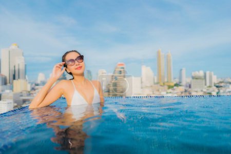 Téléchargez les photos : Portrait belle jeune femme asiatique relax heureux sourire loisirs autour de la piscine extérieure avec paysage urbain - en image libre de droit