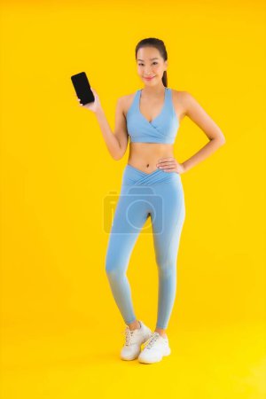 Foto de Retrato hermosa joven mujer asiática usar ropa deportiva con teléfono móvil inteligente en amarillo aislado fondo - Imagen libre de derechos