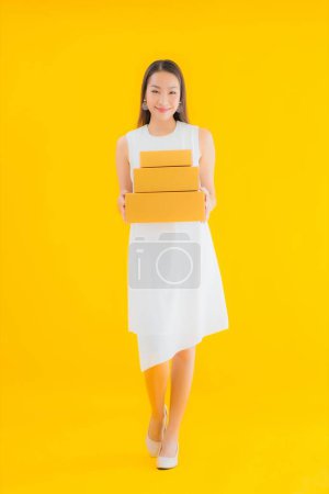 Téléchargez les photos : Portrait belle jeune femme asiatique avec boîte de colis sur fond jaune isolé - en image libre de droit