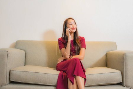 Téléchargez les photos : Portrait belle jeune femme asiatique utiliser téléphone portable intelligent sur canapé dans le salon intérieur - en image libre de droit
