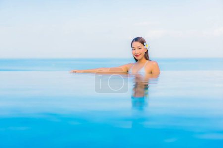 Foto de Retrato hermosa joven mujer asiática relajarse sonrisa alrededor de la piscina al aire libre en el complejo hotelero casi mar playa océano - Imagen libre de derechos