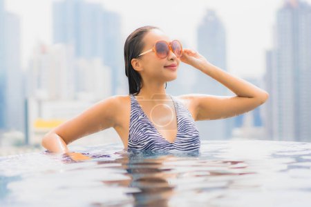 Téléchargez les photos : Portrait belle jeune femme asiatique relax sourire profiter des loisirs autour de la piscine extérieure avec vue sur la ville - en image libre de droit
