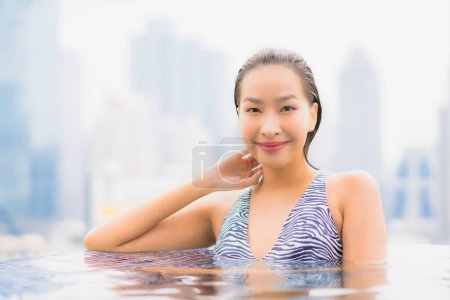 Téléchargez les photos : Portrait belle jeune femme asiatique relax sourire profiter des loisirs autour de la piscine extérieure avec vue sur la ville - en image libre de droit