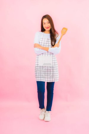 Foto de Retrato hermosa joven asiática mujer en ropa de cocina con delantal en rosa aislado fondo - Imagen libre de derechos