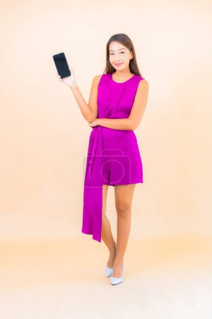 Téléchargez les photos : Portrait belle jeune femme asiatique utiliser téléphone mobile intelligent sur fond de couleur - en image libre de droit