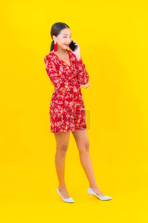 Téléchargez les photos : Portrait belle jeune femme asiatique utiliser téléphone mobile intelligent sur fond de couleur jaune - en image libre de droit