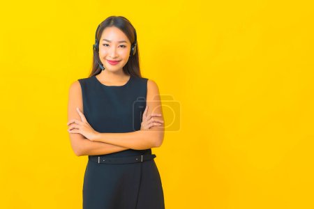 Téléchargez les photos : Portrait belle jeune femme d'affaires asiatique avec casque centre d'appel service à la clientèle sur fond jaune - en image libre de droit