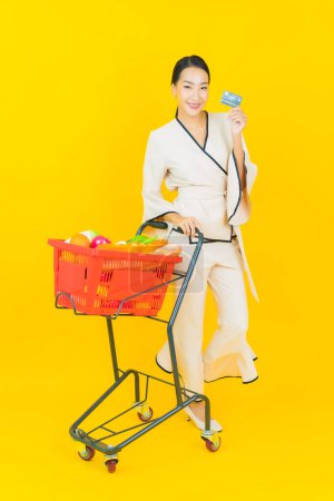 Foto de Retrato hermosa joven negocio asiático mujer con cesta de la compra de comestibles de supermercado sobre fondo amarillo - Imagen libre de derechos