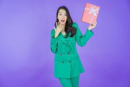 Téléchargez les photos : Portrait belle jeune femme asiatique sourire avec boîte cadeau rouge sur fond de couleur - en image libre de droit