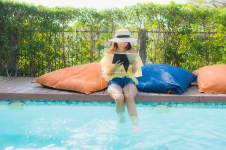 Téléchargez les photos : Portrait jeune femme asiatique lire livre autour de la piscine extérieure dans la station hôtelière - en image libre de droit