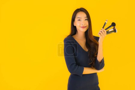 Photo for Portrait beautiful young asian woman with makeup brush on yellow isolated background - Royalty Free Image