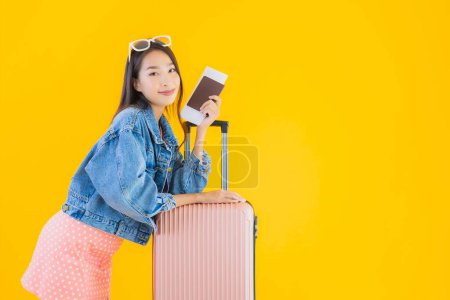 Téléchargez les photos : Portrait belle jeune femme asiatique avec bagage sac de voyage avec passeport et carte d'embarquement billet sur fond jaune isolé - en image libre de droit