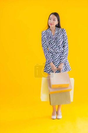 Téléchargez les photos : Portrait belle jeune femme asiatique avec sac à provisions de détail et grand magasin sur fond jaune isolé - en image libre de droit