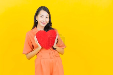 Photo for Portrait beautiful young asian woman smile with heart pillow shape on yellow color background - Royalty Free Image