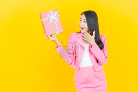 Foto de Retrato hermosa joven mujer asiática sonrisa con caja de regalo roja sobre fondo de color amarillo - Imagen libre de derechos