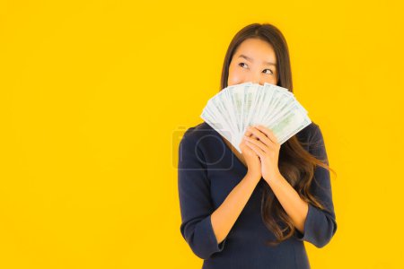 Téléchargez les photos : Portrait belle jeune femme asiatique avec de l'argent et de l'argent sur fond jaune isolé - en image libre de droit