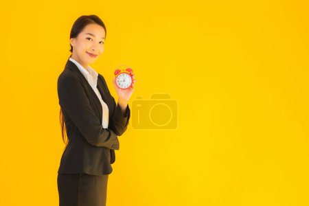 Foto de Retrato hermosa joven asiática mujer mostrar hora del reloj o alarma sobre amarillo aislado fondo - Imagen libre de derechos