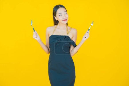 Téléchargez les photos : Portrait belle jeune femme asiatique sourire avec cuillère et fourchette sur fond de couleur - en image libre de droit