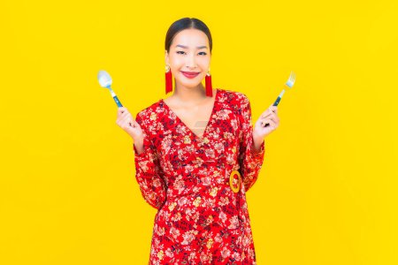 Foto de Retrato hermosa joven asiática mujer con cuchara y tenedor sobre fondo amarillo - Imagen libre de derechos