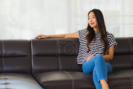 Téléchargez les photos : Portrait belle jeune femme asiatique sourire heureux se détendre sur le canapé dans le salon intérieur - en image libre de droit