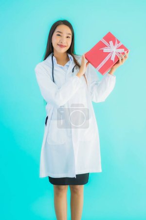 Téléchargez les photos : Portrait belle jeune asiatique médecin femme avec coffret cadeau sur fond bleu isolé - en image libre de droit