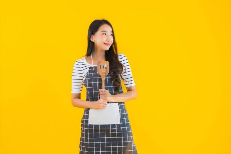 Photo for Portrait beautiful young asian woman  wear apron with black pan and Spatula on yellow isolated background - Royalty Free Image