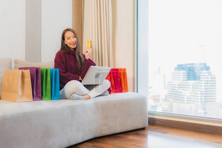 Téléchargez les photos : Portrait belle jeune femme asiatique utiliser ordinateur portable avec carte de crédit pour les achats en ligne sur le canapé - en image libre de droit