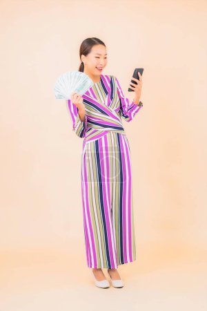 Photo for Portrait beautiful young asian woman with cash or money and mobile smart phone on color isolated background - Royalty Free Image