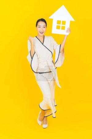 Téléchargez les photos : Portrait belle jeune femme asiatique d'affaires avec signe de papier à la maison sur fond jaune - en image libre de droit