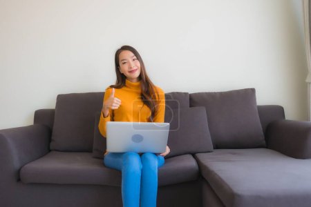 Foto de Retrato de mujer asiática joven usando portátil cuaderno de notas en el sofá para el trabajo en la sala de estar - Imagen libre de derechos