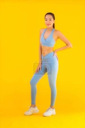 Foto de Retrato hermosa joven asiática deporte mujer con ropa deportiva listo para el ejercicio en amarillo aislado fondo - Imagen libre de derechos