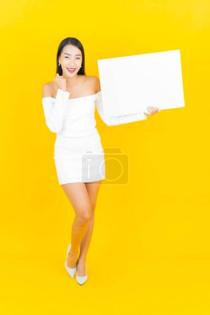 Téléchargez les photos : Portrait belle jeune femme asiatique d'affaires avec carte de panneau d'affichage blanc vide sur fond jaune - en image libre de droit