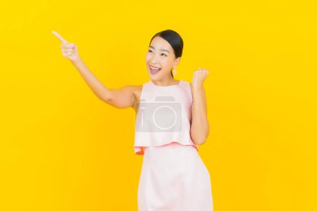 Téléchargez les photos : Portrait belle jeune femme asiatique sourire avec action sur fond de couleur jaune - en image libre de droit