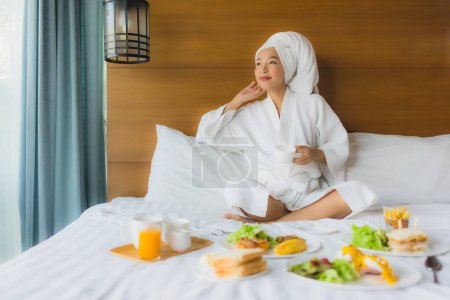 Téléchargez les photos : Portrait jeune femme asiatique sur lit avec petit déjeuner dans la chambre à coucher intérieur - en image libre de droit