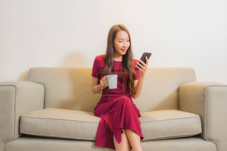 Photo for Portrait beautiful young asian woman use smart mobile phone on sofa in living room interior - Royalty Free Image