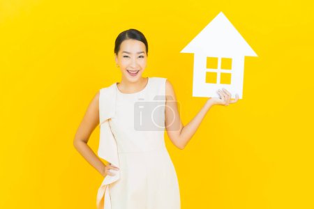 Foto de Retrato hermosa joven mujer asiática con casa o casa cartel de papel sobre fondo de color amarillo - Imagen libre de derechos