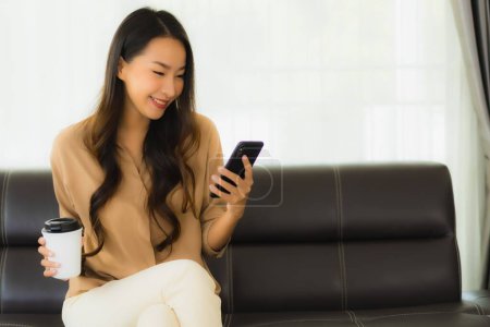 Photo for Portrait beautiful young asian woman use mobile smartphone or cellphone with coffee cup on sofa living room interior - Royalty Free Image