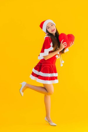 Téléchargez les photos : Portrait belle jeune asiatique vêtements de Noël et chapeau sourire heureux avec forme de coeur sur fond jaune isolé - en image libre de droit