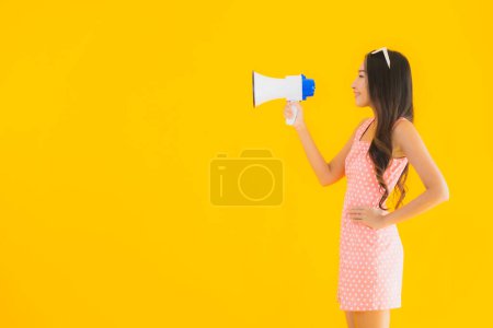 Foto de Retrato hermosa joven asiática mujer hablar alto con megáfono en amarillo aislado fondo - Imagen libre de derechos