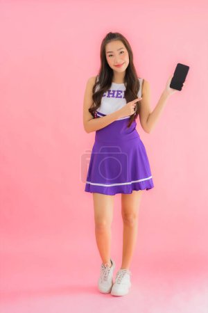 Foto de Retrato hermosa joven asiática mujer animadora uso inteligente móvil en rosa aislado fondo - Imagen libre de derechos