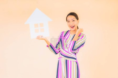 Téléchargez les photos : Portrait belle jeune femme asiatique avec maison ou maison signe papier sur fond de couleur - en image libre de droit
