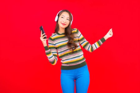 Téléchargez les photos : Portrait belle jeune femme asiatique utiliser téléphone portable intelligent avec casque pour écouter de la musique - en image libre de droit
