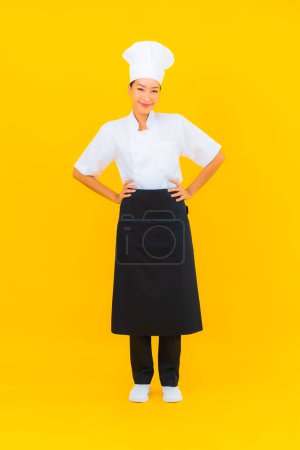 Foto de Retrato hermosa joven asiática mujer en chef o cocinero uniforme con sombrero en amarillo aislado fondo - Imagen libre de derechos