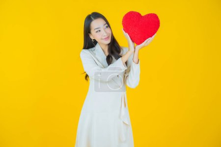 Téléchargez les photos : Portrait belle jeune femme asiatique sourire avec forme d'oreiller de coeur sur fond de couleur - en image libre de droit