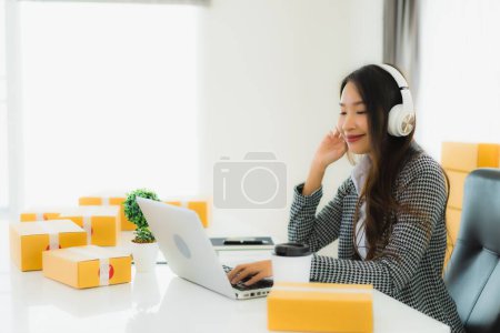 Téléchargez les photos : Portrait belle jeune femme asiatique utiliser casque pour écouter de la musique ou travailler avec ordinateur portable de l'intérieur de la maison - en image libre de droit